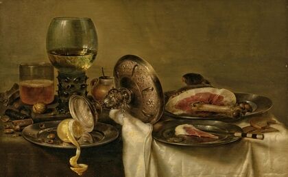 A partially draped table with an overturned tazza, roemer and glass of beer, with a partially peeled lemon and ham on pewter plates