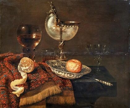 A clementine in a porcelain bowl, a nautilus cup, a roemer, two glasses, a knife, a peeled lemon on an ornamental carpet on a table