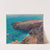 A rocky coast, in the background a sailing boat by Hans Wilt