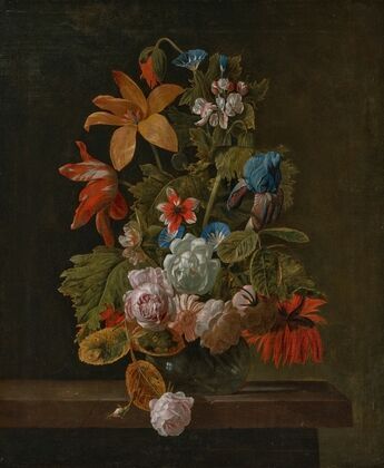Tulips, roses, an iris and various flowers in a glass vase on a stone ledge